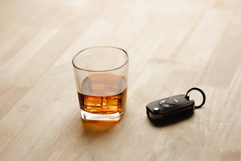A glass of liquor next to a set of car keys.