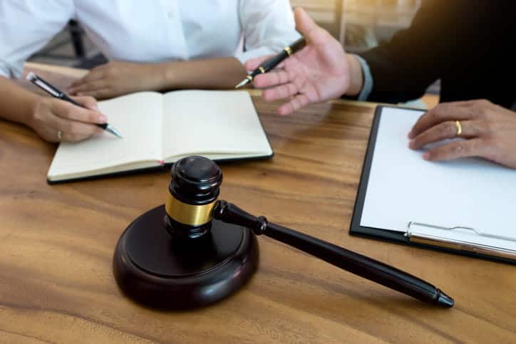 A medical malpractice lawyer discussing a case with their client. In front of them is paperwork and a gavel. 