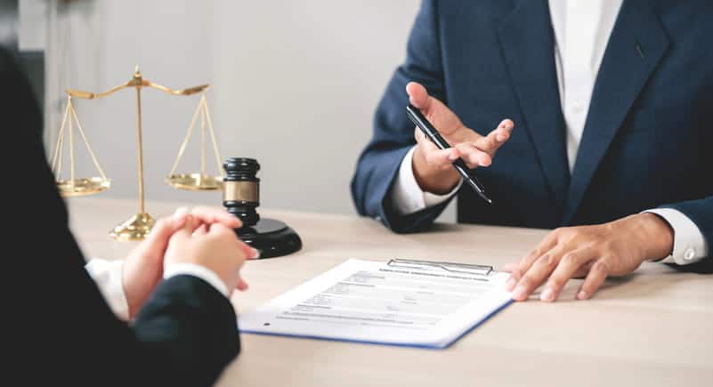 A personal injury lawyer reviewing paperwork with their client. Next to them is the scales of justice and a gavel.