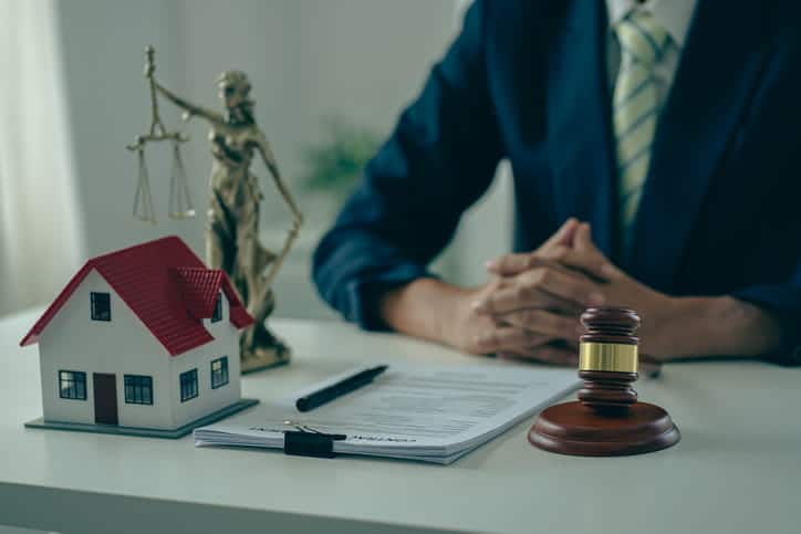 A rental injury attorney sits at his desk with paperwork, a gavel, the lady justice statue and a model of a rented house in front of him.