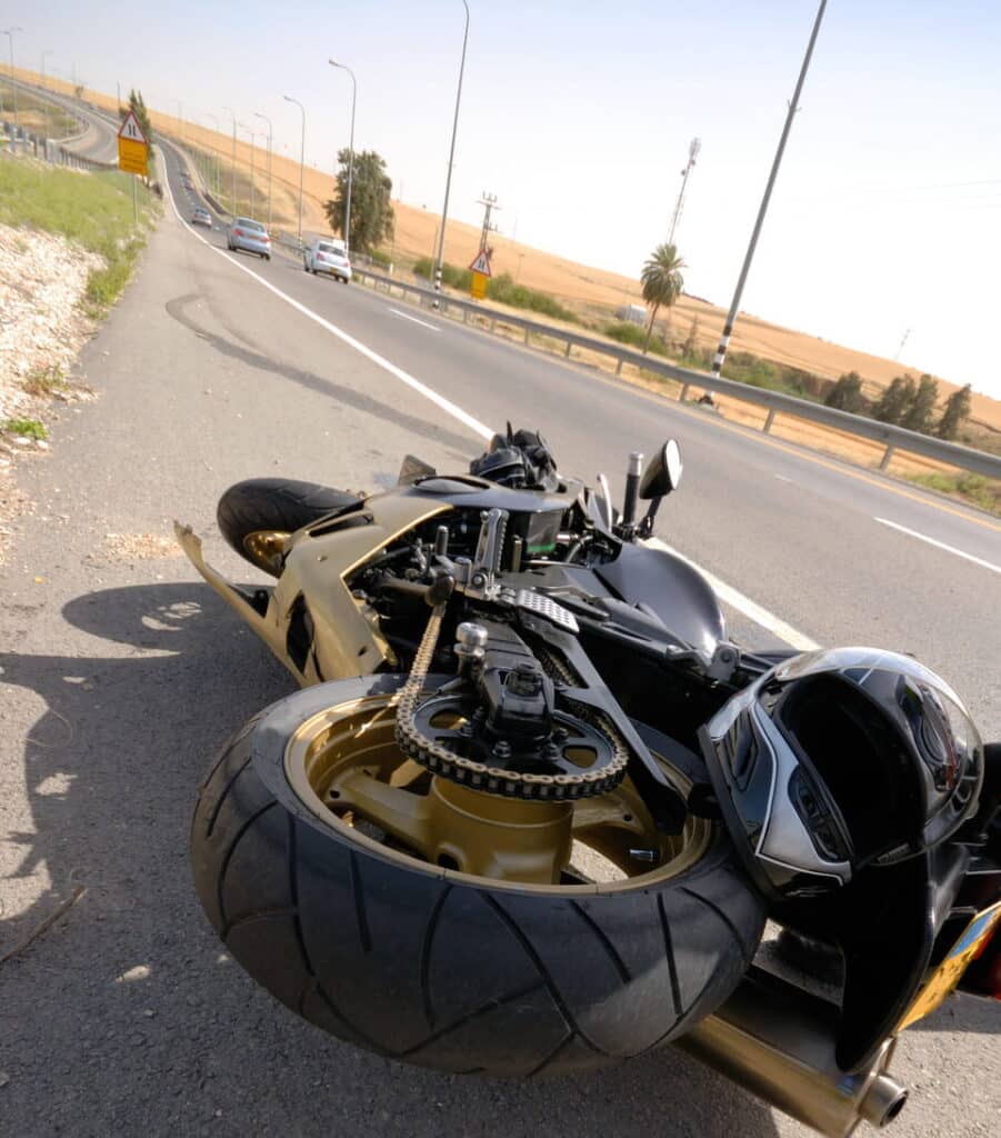 A tipped over motorcycle along with a helmet on the side of a road after a motorcycle accident.