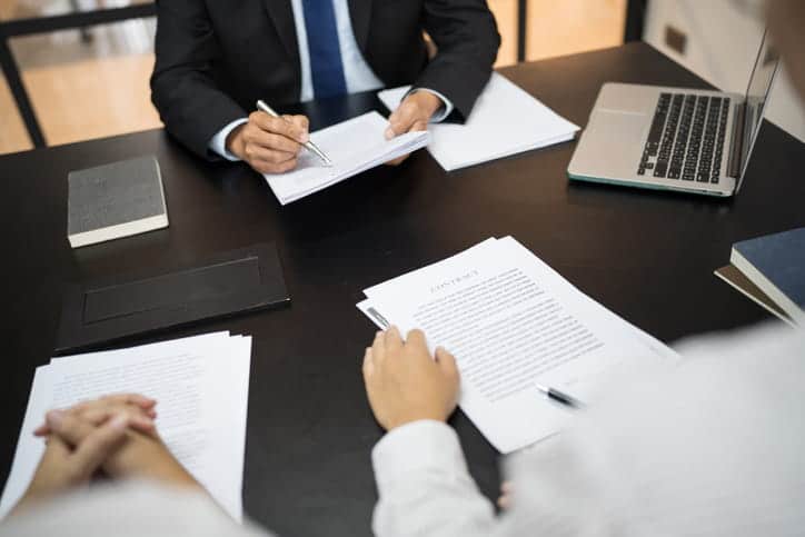 Elevator And Escalator Malfunction Injuries 2 A personal injury lawyer reviewing paperwork with his two clients. On his desk is more paperwork, a book, and an open laptop.