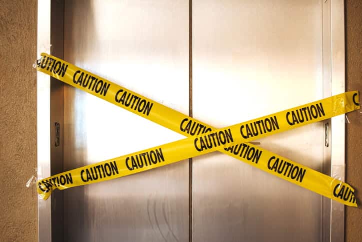 A broken elevator with yellow caution tape taped across the closed doors.