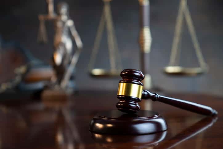 The focus is on a gavel on a car accident attorney's desk. In the background out of focus is a Lady Justice statue and the scales of justice. 