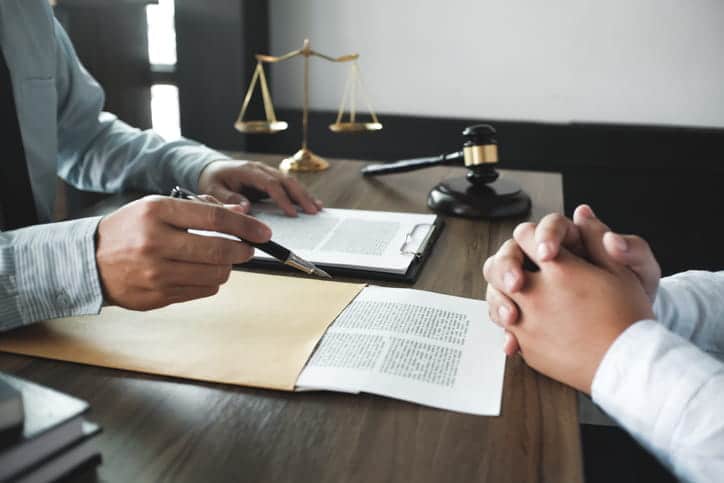 Are All Rear-End Accidents At-Fault? 2 A car accident lawyer discussing a case with his client. Between them is paperwork, the scales of justice and a gavel.