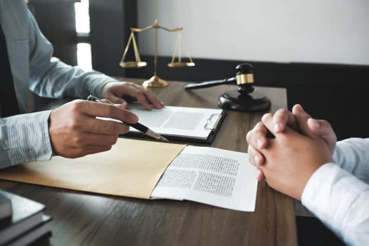 A car accident lawyer discussing a case with his client. Between them is paperwork, the scales of justice and a gavel. 