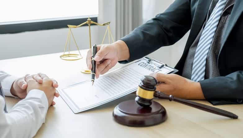 A car accident lawyer is reviewing a contract with their client. Next to them are the scales of justice and a gavel. 