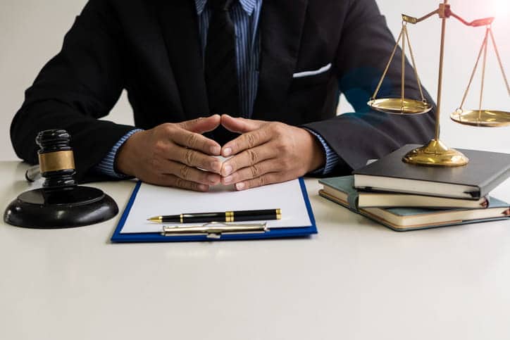 A catastrophic injury lawyer sitting at this desk. In front of him is a gavel, paperwork with a pen, and a stack of books with the scales of justice sitting on top of them. 