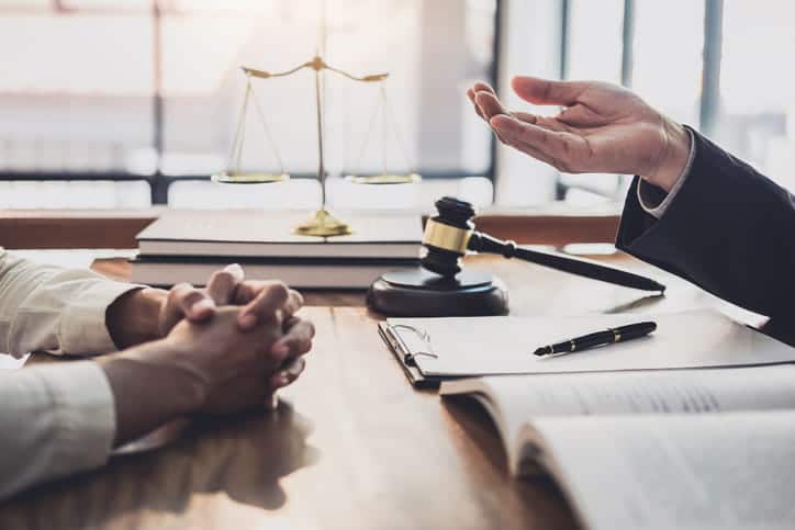 A premises liability lawyer is discussing a case with his client. In front of him is paperwork, a gavel, and the scales of justice on a stack of books.