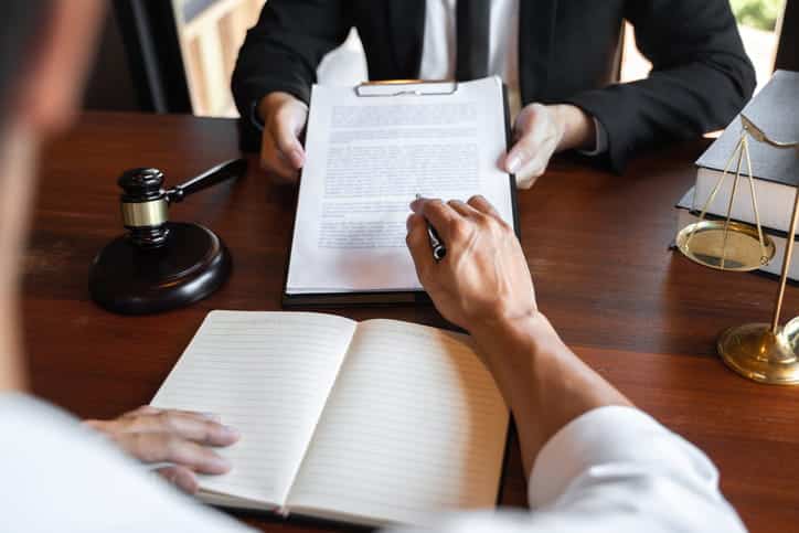 An Airbnb injury lawyer reviewing paperwork with his client. In front of him is a blank notebook, a gavel, and the scales of justice. 