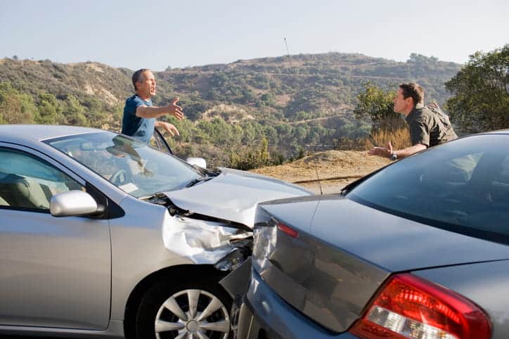 Two male drivers arguing with each other outside their cars after a rear-end collision.