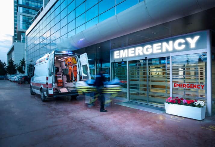 Paramedics wheeling a stretcher from an ambulance into an emergency room. 