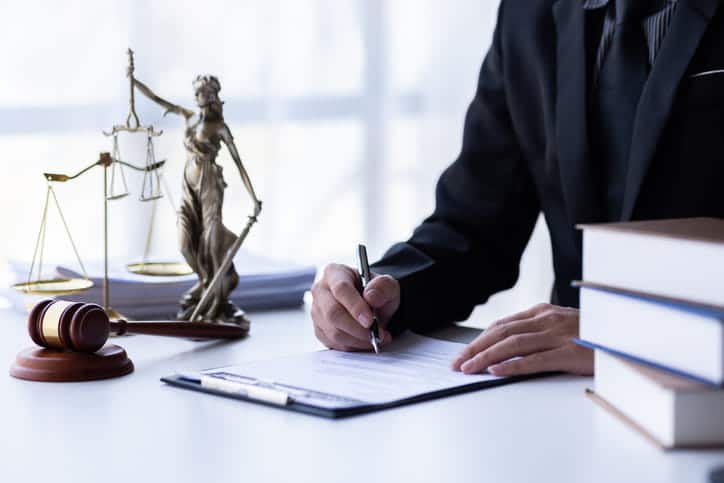 When Is A Car Considered Totaled? 2 A car accident lawyer working on paperwork at his desk with a stack of books, a lady justice statue, the scales of justice and a gavel next to him.