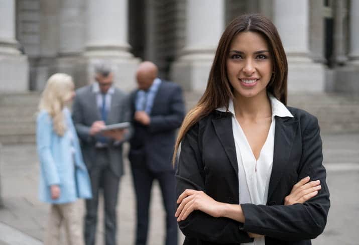 A medical malpractice lawyer with her arms crossed, smiling for the camera. Behind her are three attorneys blurred out in the background. 