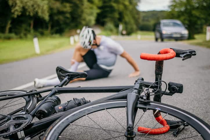 A bicyclist clutching his leg in pain with his bike tipped over in the roadway after being in a hit-and-run accident.