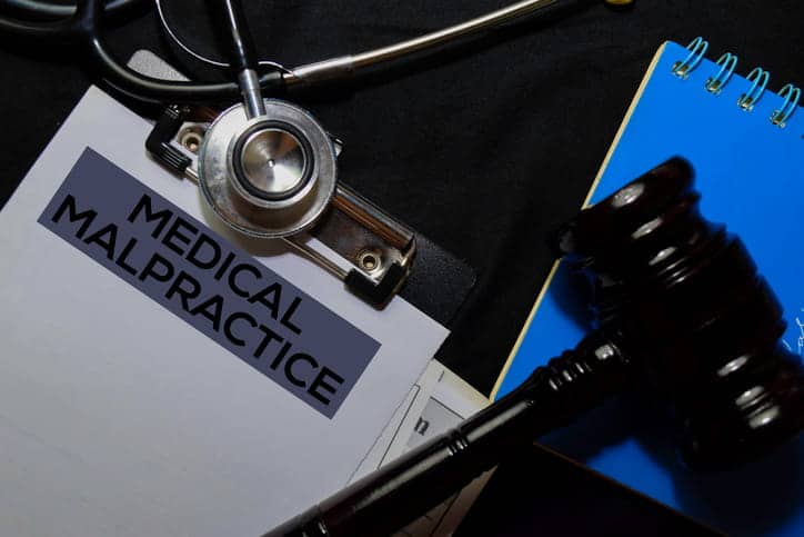 A clipboard that reads "medical malpractice" with a stethoscope and a gavel on top of it.
