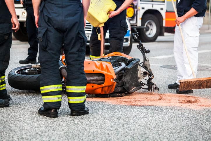 A crashed motorcycle in the road with emergency personnel standing around it.