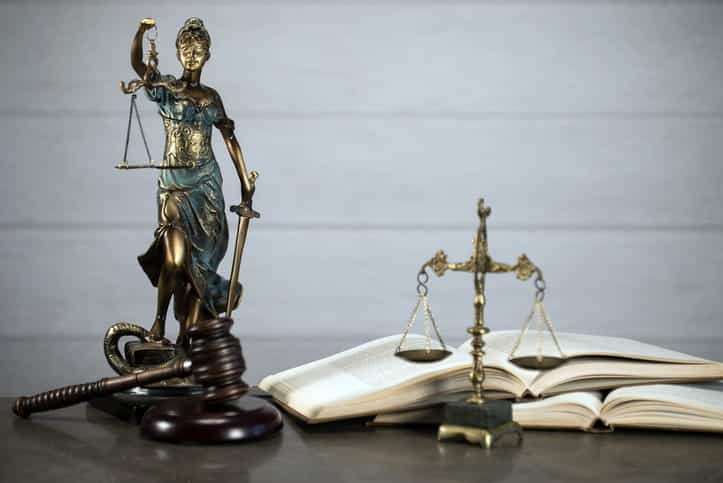 A Lady Justice statue, a gavel, and open book, and the scales of justice on a motorcycle accident injury attorney's desk.
