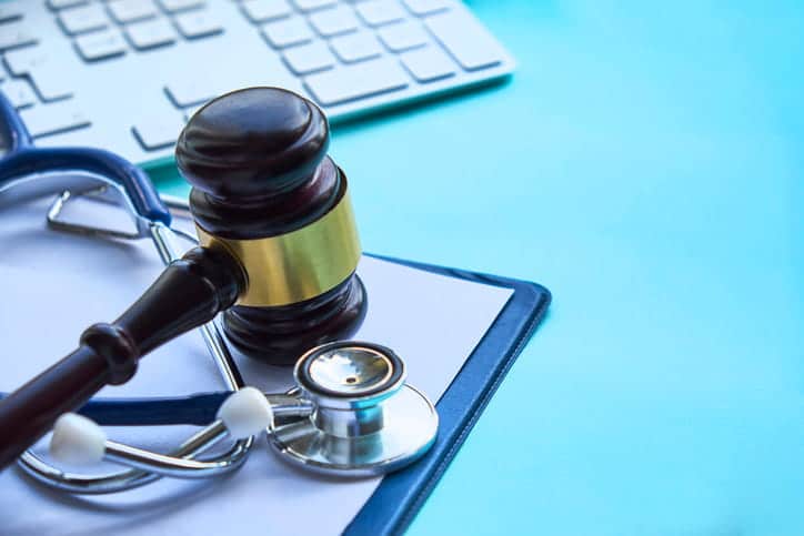 A gavel over top a stethoscope and a clipboard. 