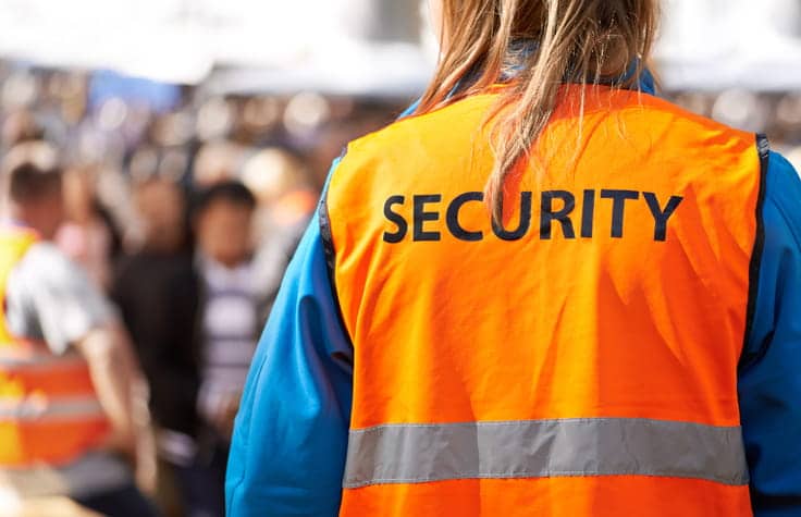 The back of a person wearing an orange vest that reads: "Security." They are helping with crowd control at an event. 