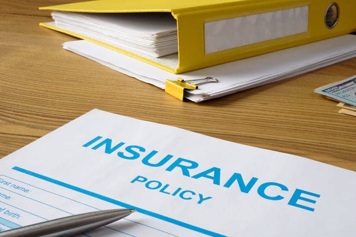 A form that reads "Insurance Policy" in front of a yellow binder.