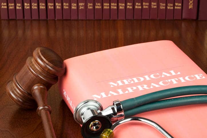 A book that reads: "medical malpractice" next to a gavel with a stethoscope on top.