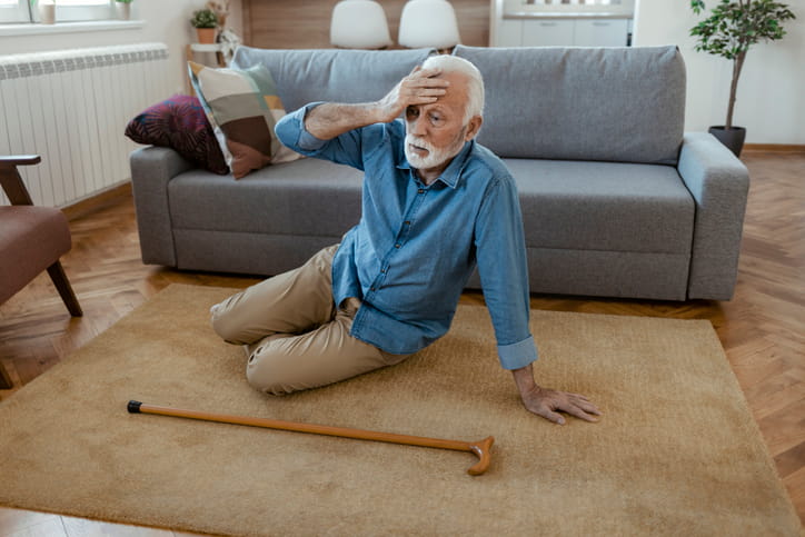 A man holding his head with his cane next to him after he fell in his apartment.