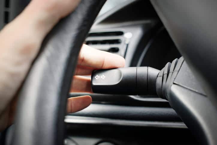 A person turning on their left blinker in the car to signal a lane change.