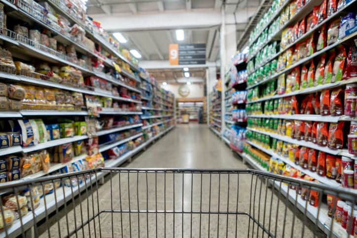 Focus is on a grocery cart going down the aisle at a grocery store.
