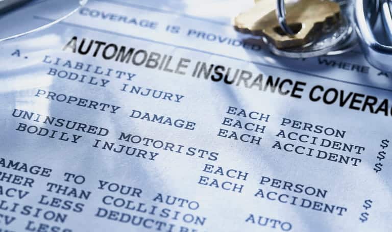 A close up of an automobile insurance coverage document with a set of car keys on top of it.