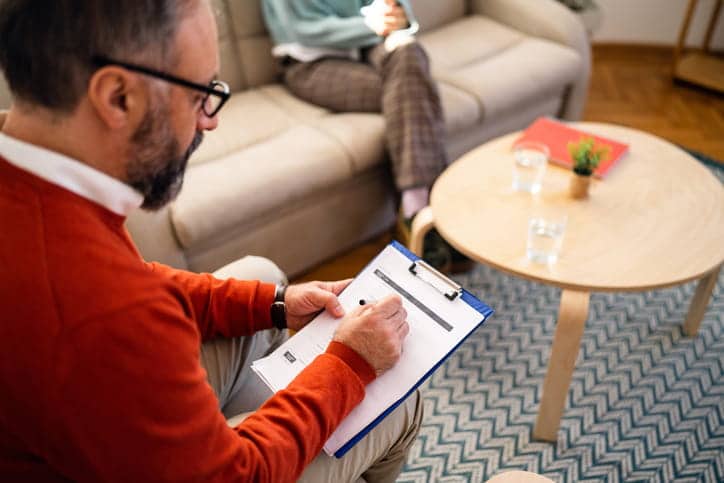 Therapist Malpractice Lawyers 1 A therapist taking notes as he speaks to a client who is sitting on the couch.