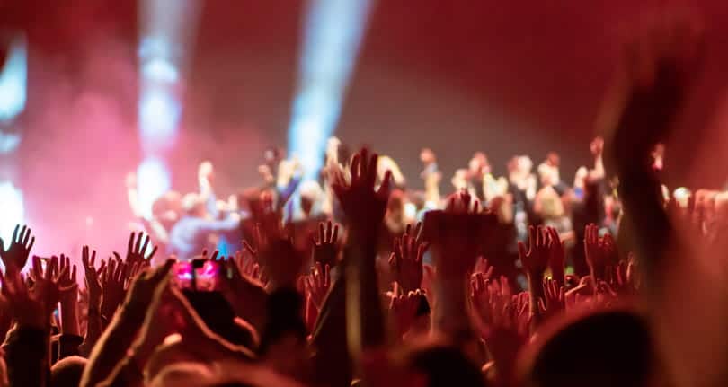 An overcrowded venue showing the crowd raising their hands as they listen to a performance.