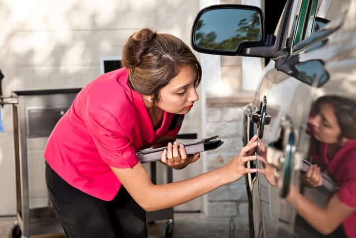 A woman with a tablet examining vehicle damage after an accident.