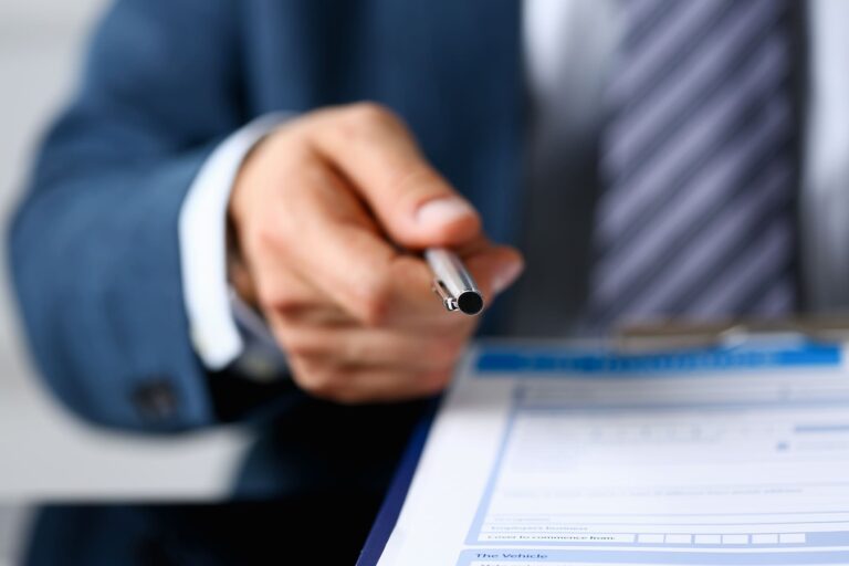 Car Accident Interview Questions And Answers 1 An attorney handing a pen to a client to write down the answers to their car accident questions.
