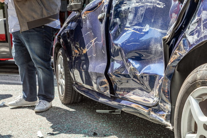 A person standing next to their damaged vehicle after being in a car accident.