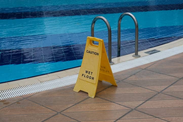 A wet floor caution sign sits next to a hotel swimming pool.