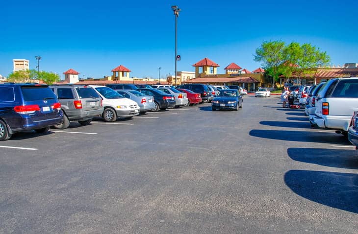 A car driving through a busy parking lot that's full of parked cars.