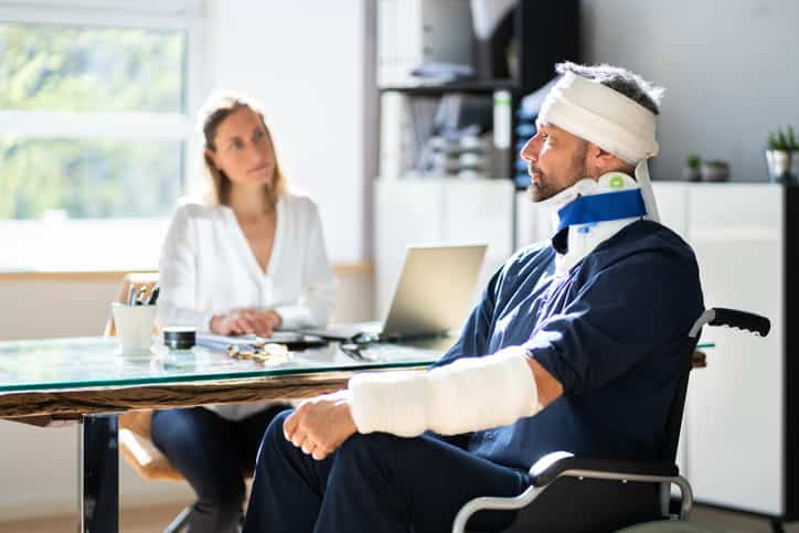 Green Valley Personal Injury Attorney 1 A man with his head and arm wrapped while wearing a neck brace sits in a wheelchair as his personal injury attorney discusses his case.