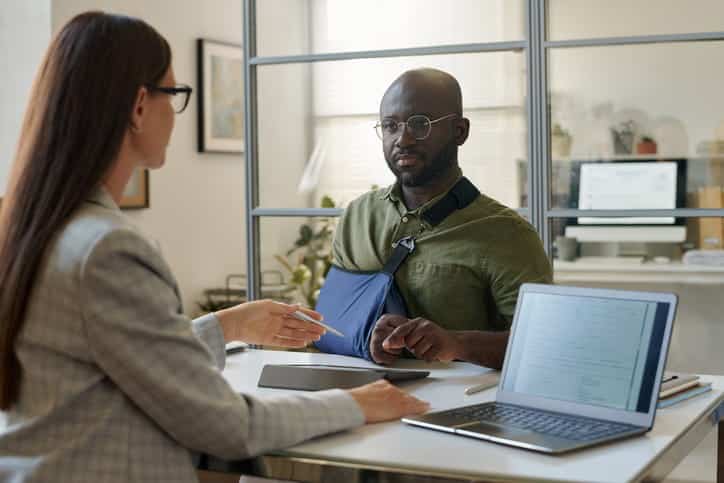 A personal injury attorney discusses a case with their client who is in an arm sling.