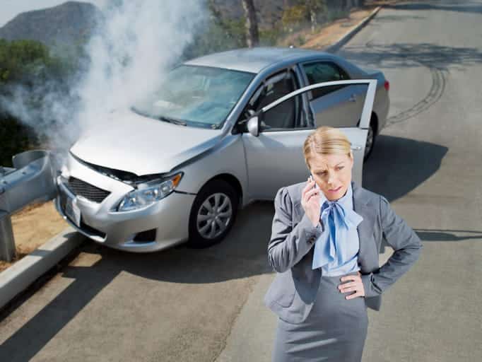 Aventura 13 A woman on the phone after a car accident with her damaged vehicle behind her.