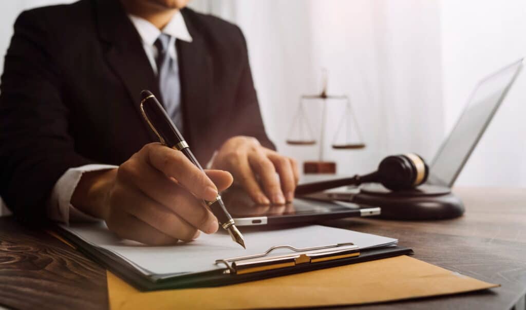 Henderson Spinal Cord Injury 2 A personal injury attorney works on paperwork at his desk. Next to him is the scales of justice an open laptop and a gavel 1024x604 1