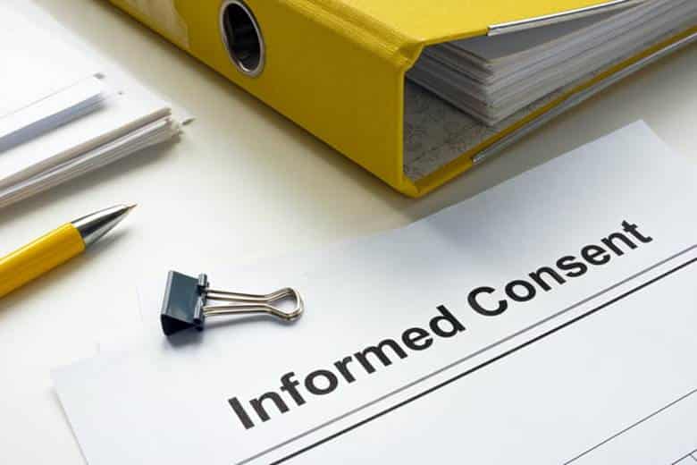 A piece of paper that reads "informed consent" next to a yellow binder.