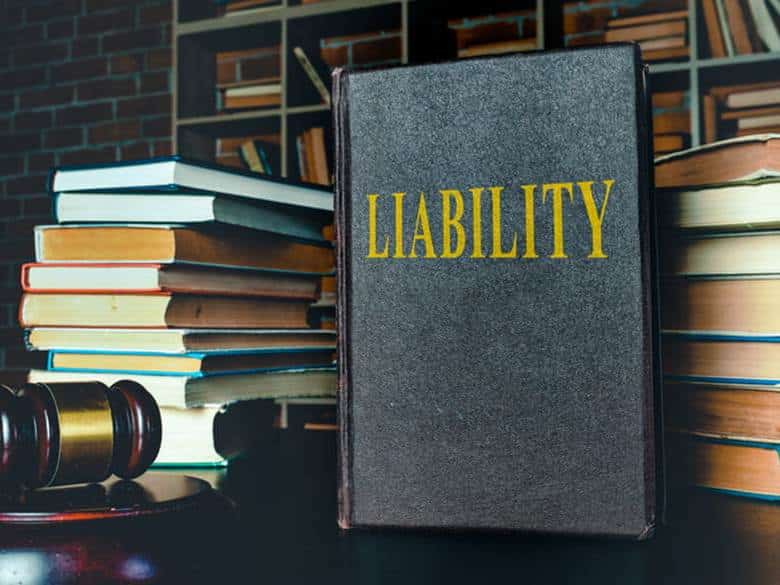 A stack of books next to a gavel, with one that's titled "liability. "
