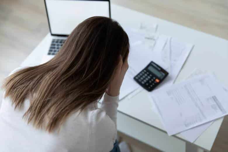 A woman holding her head in frustration as she looks at overdue bills due to lost wages after a car accident.